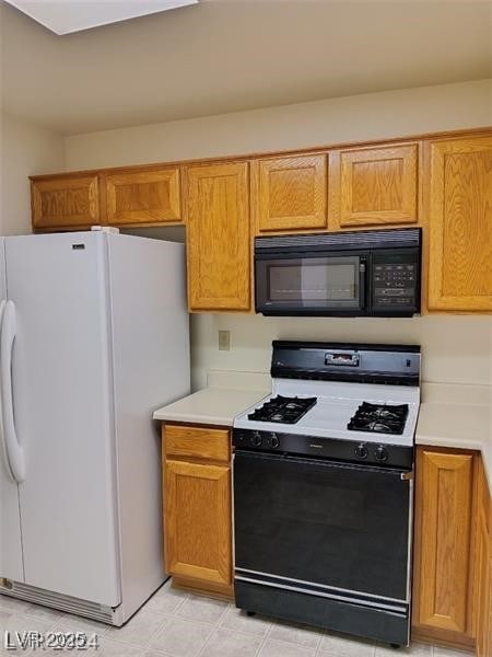 kitchen with freestanding refrigerator, black microwave, gas range, light countertops, and brown cabinets