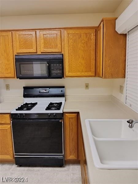 kitchen featuring black microwave, light countertops, a sink, light tile patterned flooring, and gas range oven