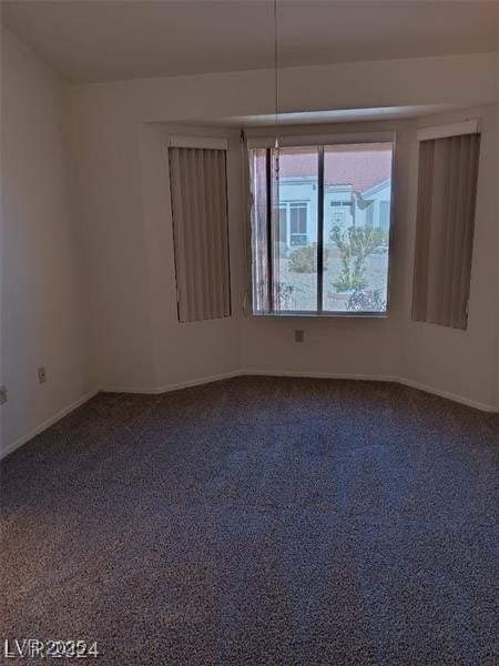 spare room featuring dark colored carpet and baseboards