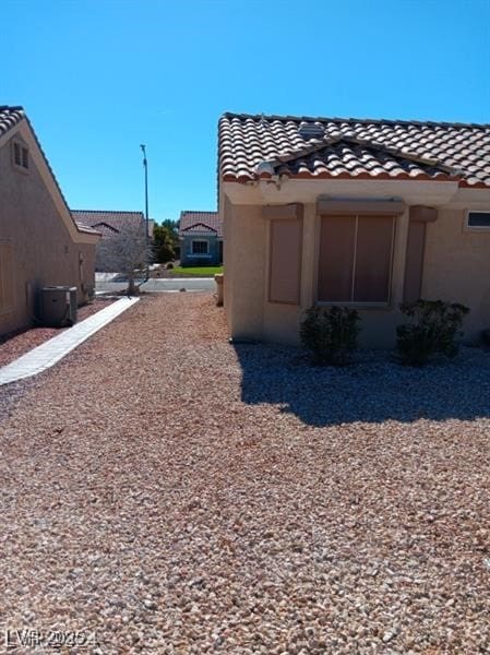 view of side of property with central air condition unit, a tiled roof, and stucco siding