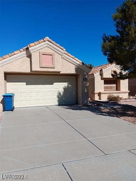 view of front of house featuring a tiled roof, an attached garage, stucco siding, and driveway