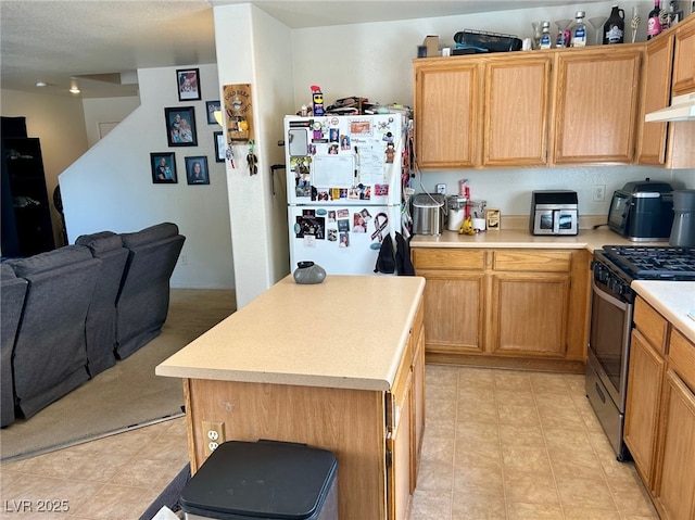 kitchen featuring freestanding refrigerator, open floor plan, stainless steel range with gas cooktop, light countertops, and under cabinet range hood