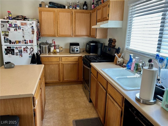 kitchen featuring a sink, stainless steel gas range oven, light countertops, freestanding refrigerator, and under cabinet range hood