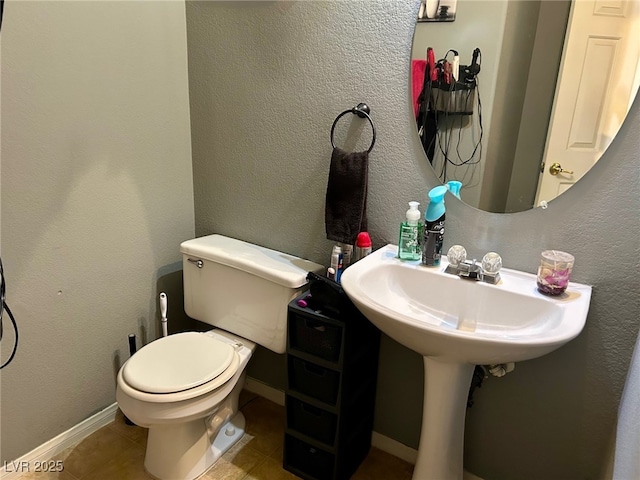 bathroom with baseboards, tile patterned flooring, a textured wall, and toilet