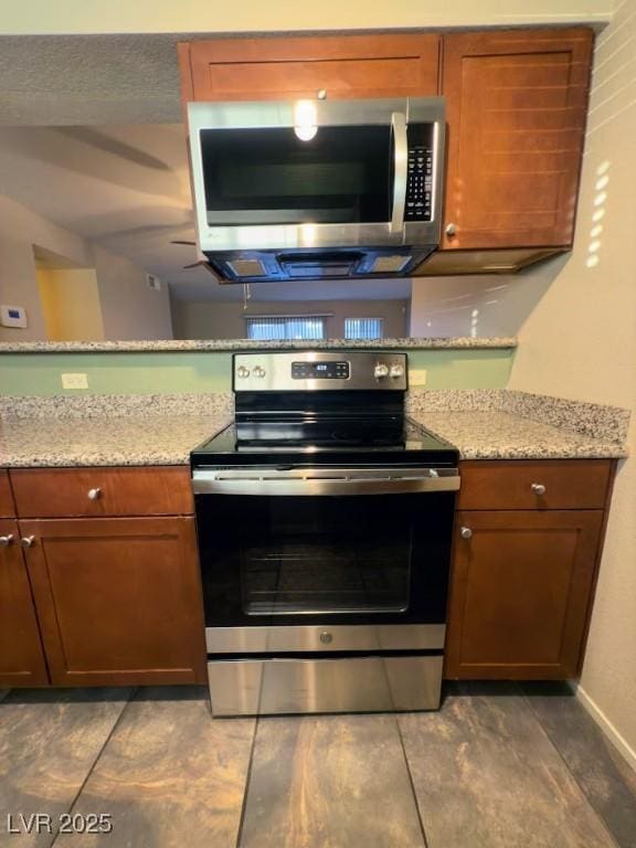 2750 S Durango Dr Unit 1038, Las Vegas, NV 89117 - kitchen featuring baseboards, light stone counters, brown cabinets, and stainless steel appliances