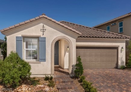 mediterranean / spanish-style home featuring a tiled roof, an attached garage, driveway, and stucco siding