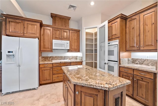kitchen with brown cabinetry, a kitchen island, white appliances, and visible vents