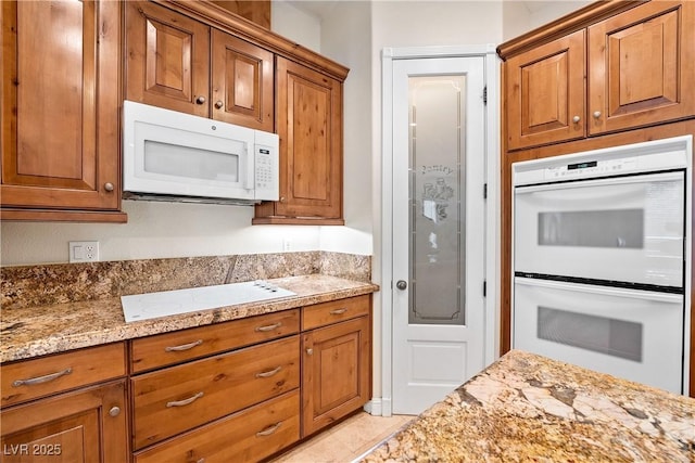 kitchen with brown cabinets, white appliances, and light stone countertops