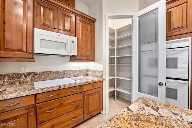 kitchen with brown cabinets, white appliances, and light stone countertops