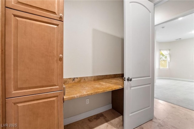 interior space with baseboards, built in desk, and light carpet