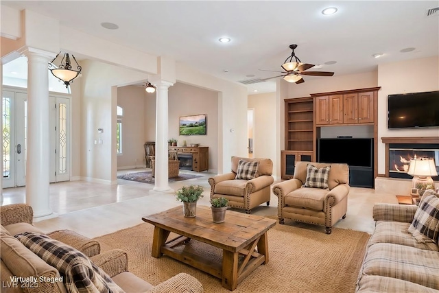 living room with ornate columns, a glass covered fireplace, visible vents, and ceiling fan