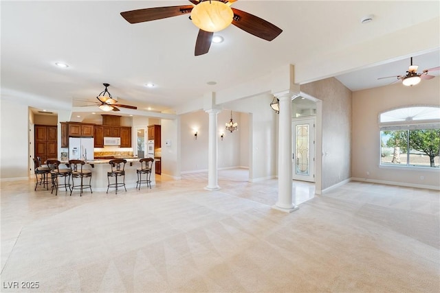 living area with ornate columns, baseboards, ceiling fan, and light colored carpet