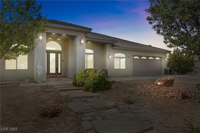 view of front of house with an attached garage, a tile roof, stucco siding, french doors, and driveway