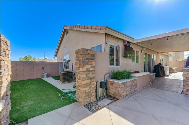 view of side of home with a patio, a fenced backyard, central AC, and stucco siding