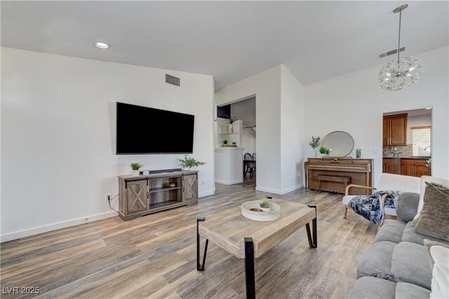 living area with baseboards, visible vents, an inviting chandelier, and light wood-style flooring