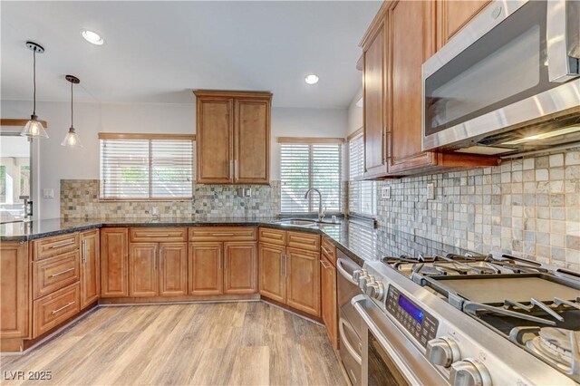 kitchen with brown cabinetry, tasteful backsplash, a sink, dark stone countertops, and stainless steel appliances
