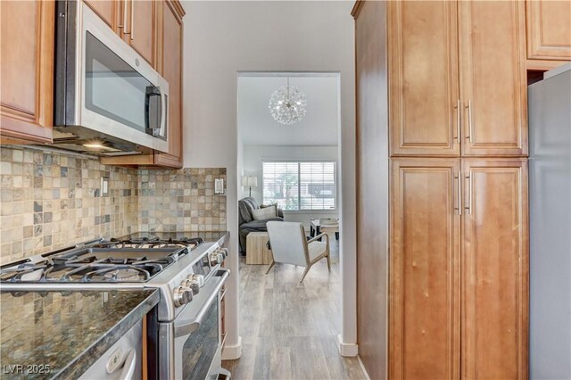 kitchen with appliances with stainless steel finishes, an inviting chandelier, dark stone countertops, wood finished floors, and tasteful backsplash