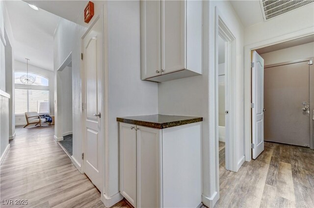 corridor with a chandelier, baseboards, visible vents, and light wood-style floors