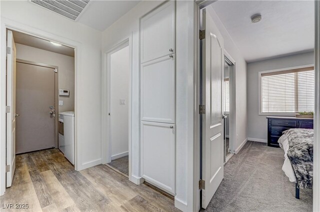 hallway with baseboards, visible vents, and light wood finished floors