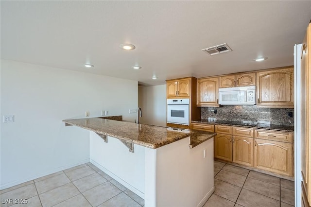 3111 Bel Air Dr Unit 18B, Las Vegas, NV 89109 - kitchen with visible vents, a peninsula, white appliances, a breakfast bar, and light tile patterned floors
