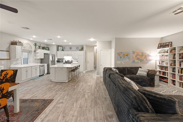 living area with ceiling fan, recessed lighting, visible vents, and light wood-style floors