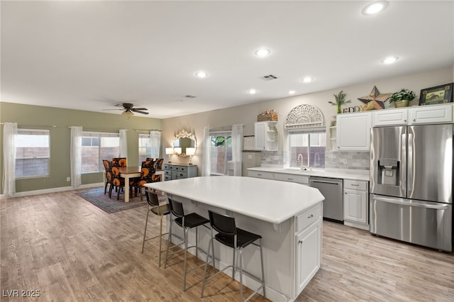 kitchen featuring light wood finished floors, a sink, stainless steel appliances, a kitchen breakfast bar, and visible vents