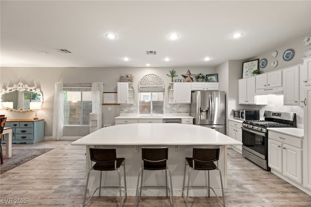 kitchen with under cabinet range hood, stainless steel appliances, visible vents, and a kitchen island
