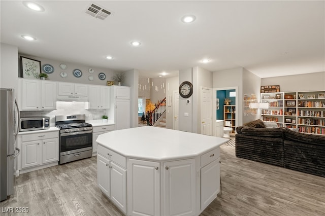 kitchen featuring light wood-style flooring, a center island, under cabinet range hood, visible vents, and appliances with stainless steel finishes