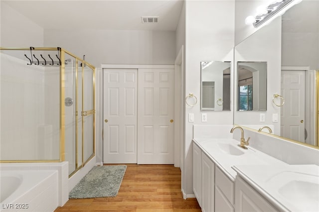 bathroom with double vanity, wood finished floors, a sink, visible vents, and a shower stall