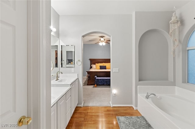 ensuite bathroom with a ceiling fan, ensuite bathroom, a garden tub, vanity, and wood finished floors