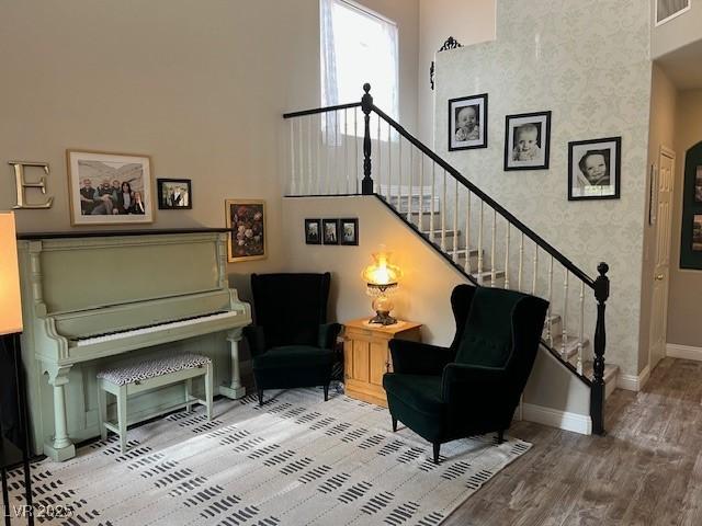 sitting room featuring wood finished floors, visible vents, baseboards, a towering ceiling, and stairs