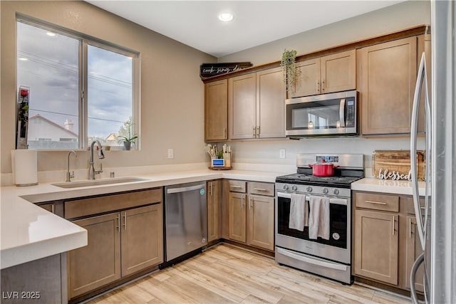 kitchen with appliances with stainless steel finishes, light wood-type flooring, a sink, light countertops, and recessed lighting