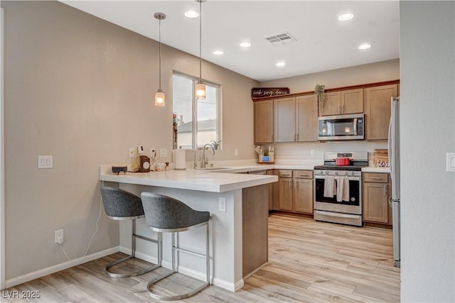 kitchen featuring a peninsula, appliances with stainless steel finishes, visible vents, and light wood-style floors