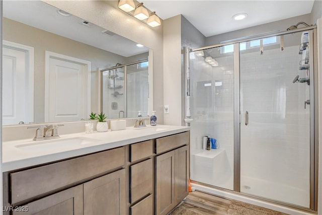 full bathroom with a sink, double vanity, a shower stall, and wood finished floors