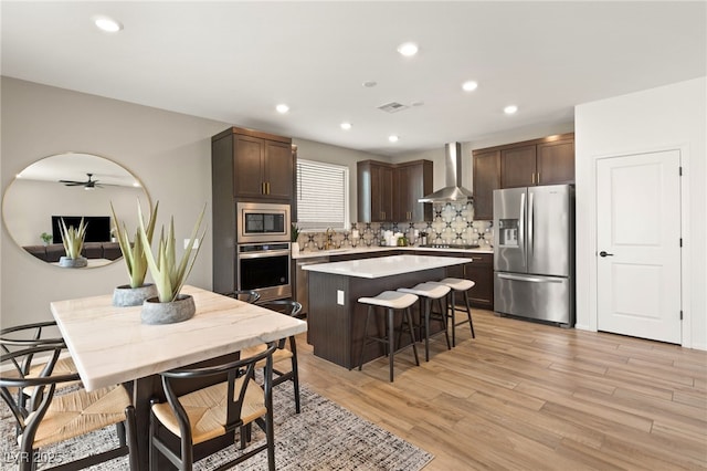 kitchen with dark brown cabinetry, a breakfast bar area, a center island, tasteful backsplash, and appliances with stainless steel finishes