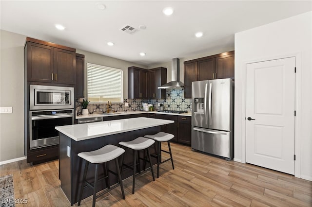 kitchen featuring a sink, a breakfast bar area, wall chimney exhaust hood, stainless steel appliances, and visible vents