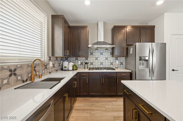 kitchen with wall chimney range hood, light countertops, tasteful backsplash, a sink, and appliances with stainless steel finishes