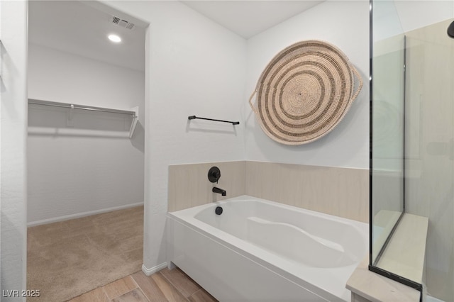 bathroom featuring a walk in closet, baseboards, wood finished floors, visible vents, and a garden tub