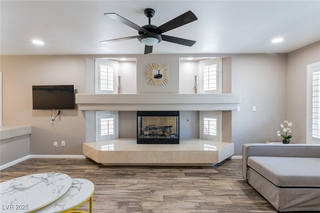 living area featuring a fireplace with raised hearth, ceiling fan, recessed lighting, and wood finished floors