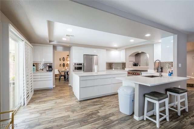 kitchen with decorative backsplash, modern cabinets, white cabinetry, arched walkways, and appliances with stainless steel finishes