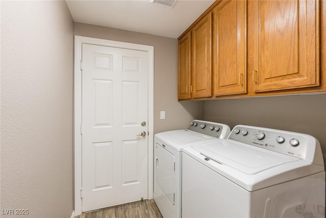 clothes washing area with washing machine and clothes dryer, visible vents, light wood-type flooring, and cabinet space