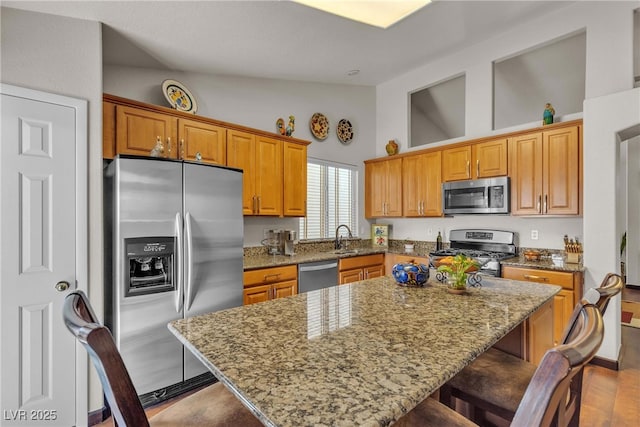 kitchen with high vaulted ceiling, a breakfast bar, stainless steel appliances, and light stone countertops