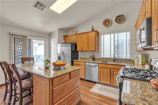 kitchen featuring a kitchen bar, visible vents, vaulted ceiling, a sink, and stainless steel appliances