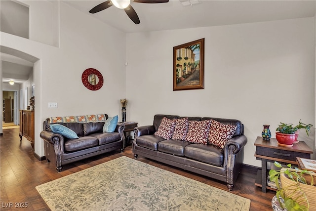 living room featuring arched walkways, ceiling fan, baseboards, and dark wood-style flooring