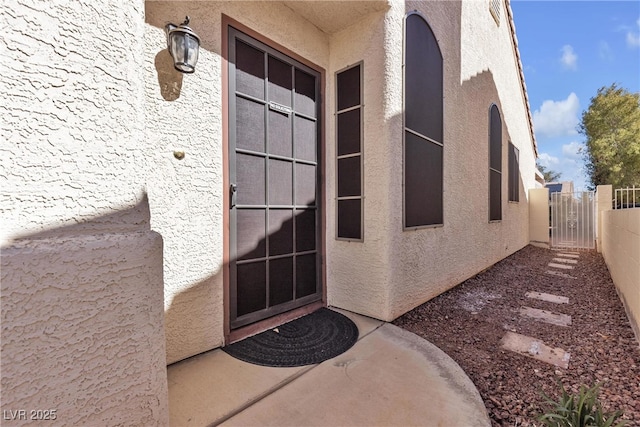 doorway to property featuring a gate, stucco siding, and fence