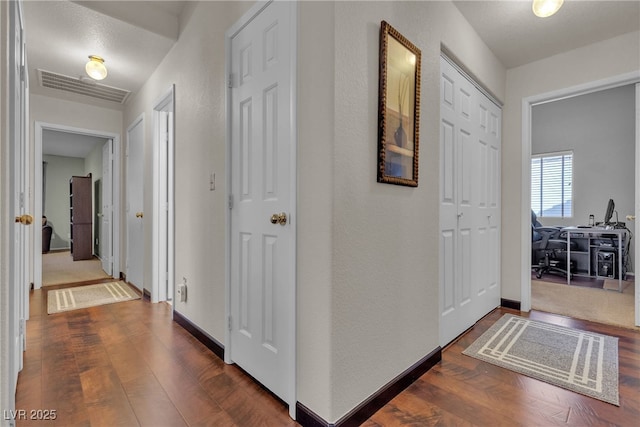 hall featuring visible vents, baseboards, and dark wood-type flooring