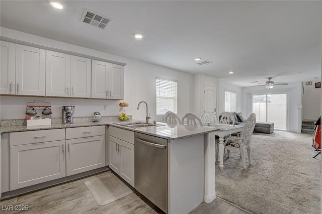 kitchen with light stone counters, a sink, dishwasher, a peninsula, and visible vents