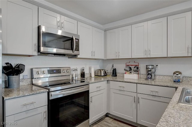 kitchen with white cabinets, appliances with stainless steel finishes, light stone counters, a sink, and light wood finished floors