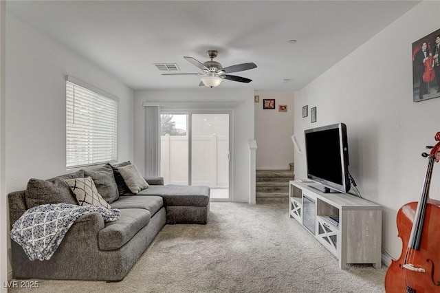 carpeted living area with visible vents, stairs, and ceiling fan