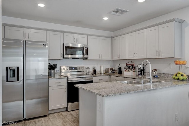 kitchen with light stone counters, a sink, stainless steel appliances, a peninsula, and visible vents